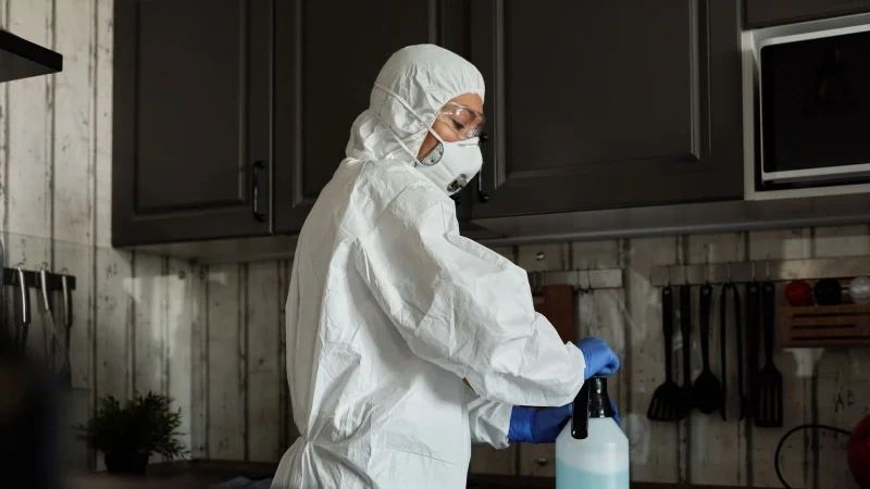 Technician in protective gear with a spray bottle during dead rodent removal